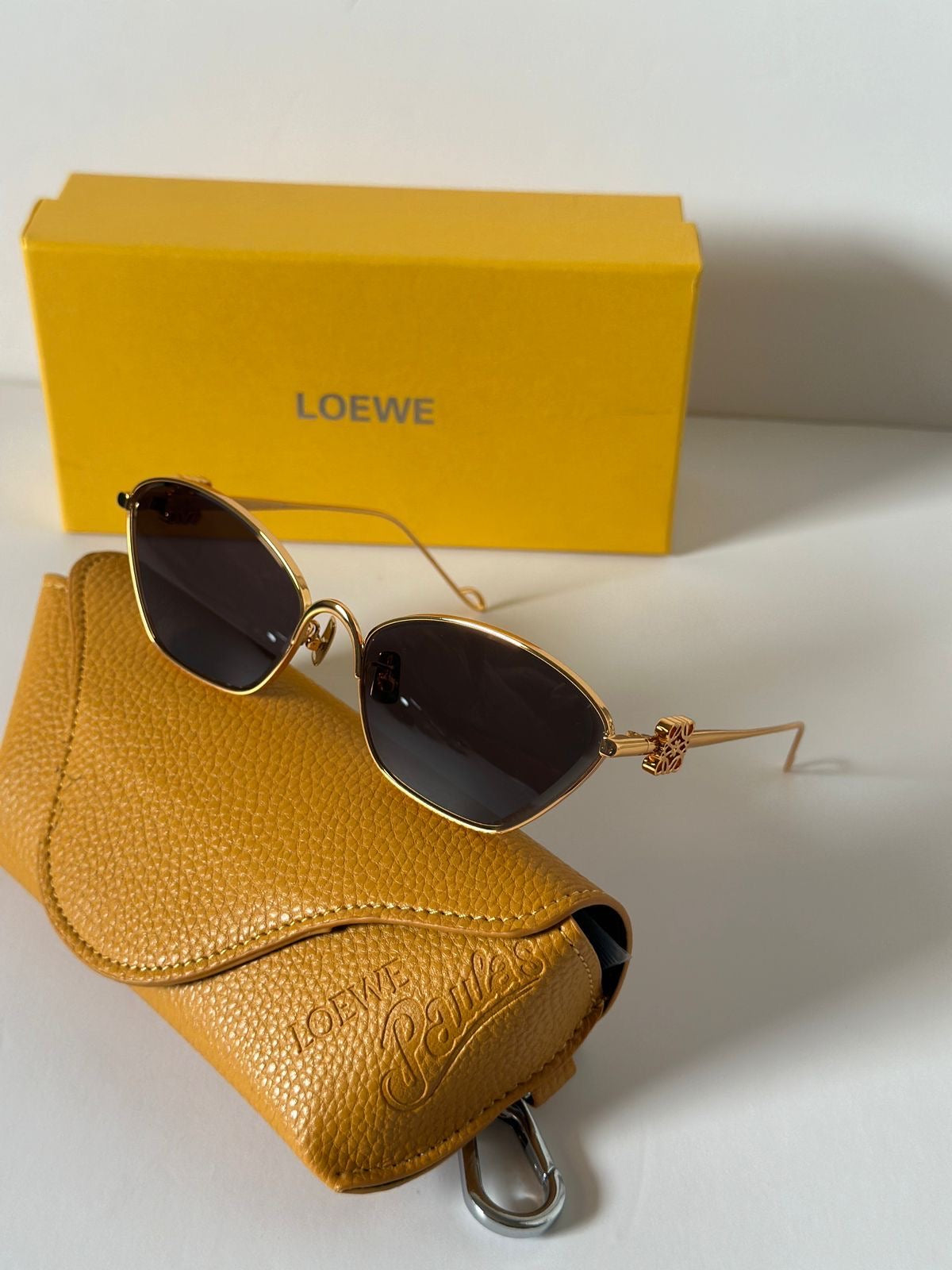 Gold sunglasses with dark lenses on a yellow case, next to a Loewe box.