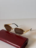 Gold-framed sunglasses with brown lenses on a Gucci case against a light background