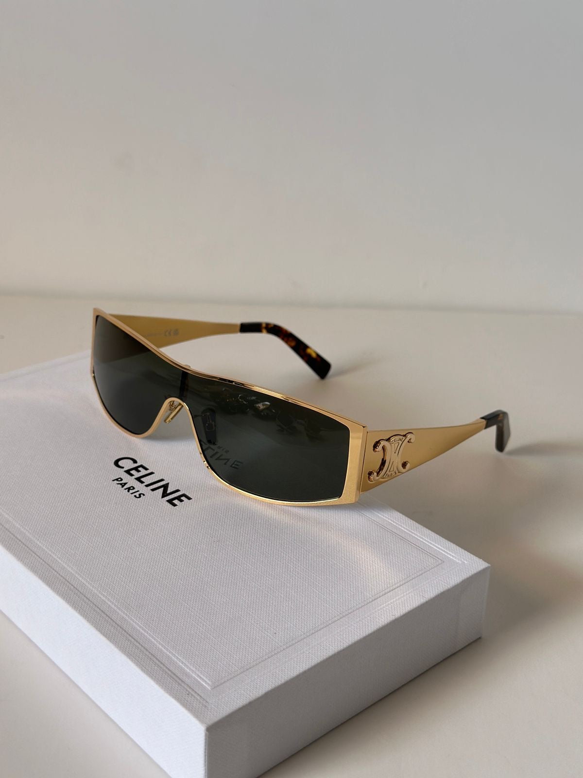 Celine sunglasses with gold metal frames, dark lenses, and tortoiseshell temple tips, resting on a white Celine box.