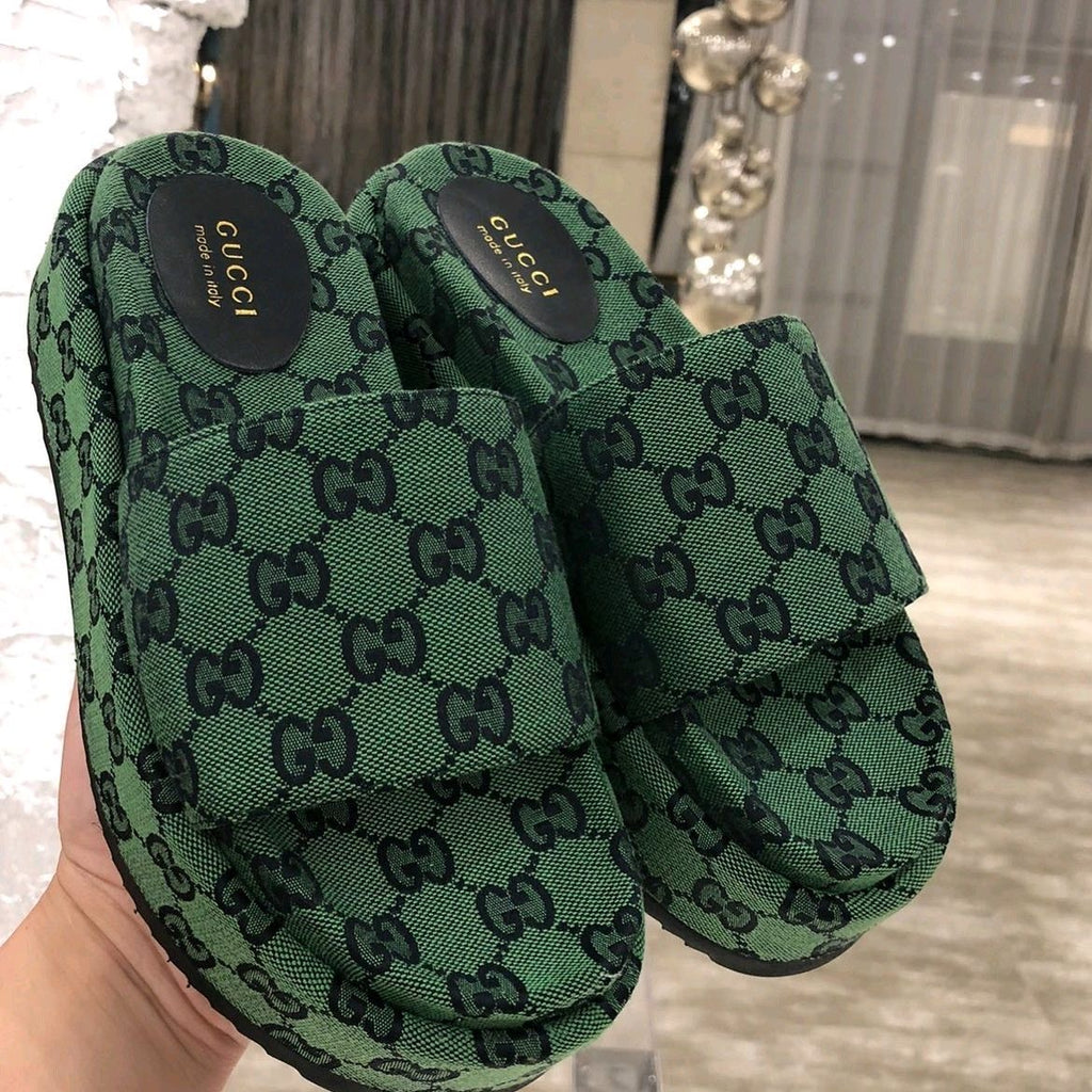 Green Gucci slider sandals held in a hand with a blurred indoor background