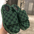 Green Gucci slider sandals held in a hand with a blurred indoor background