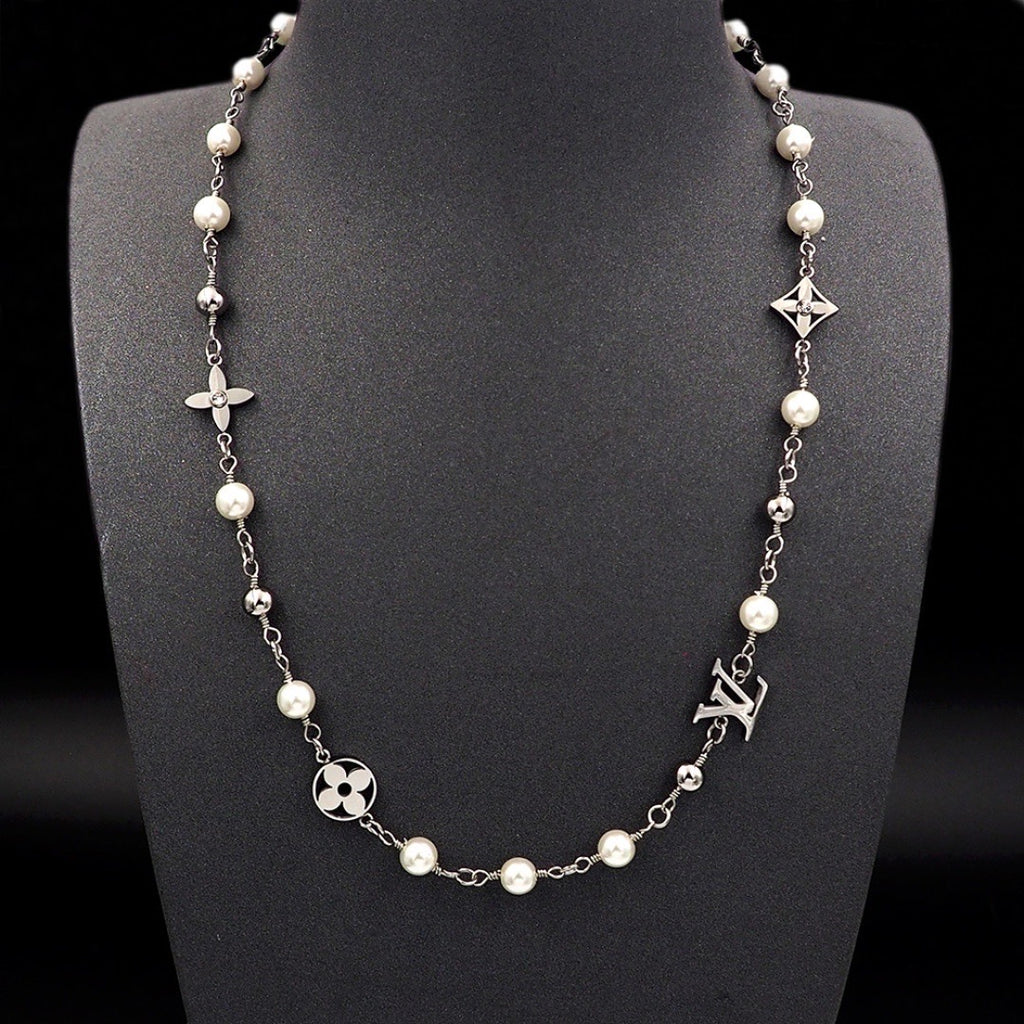 A silver-tone chain necklace with white faux pearls and Louis Vuitton monogram and floral motifs, displayed on a black mannequin bust against a black background.