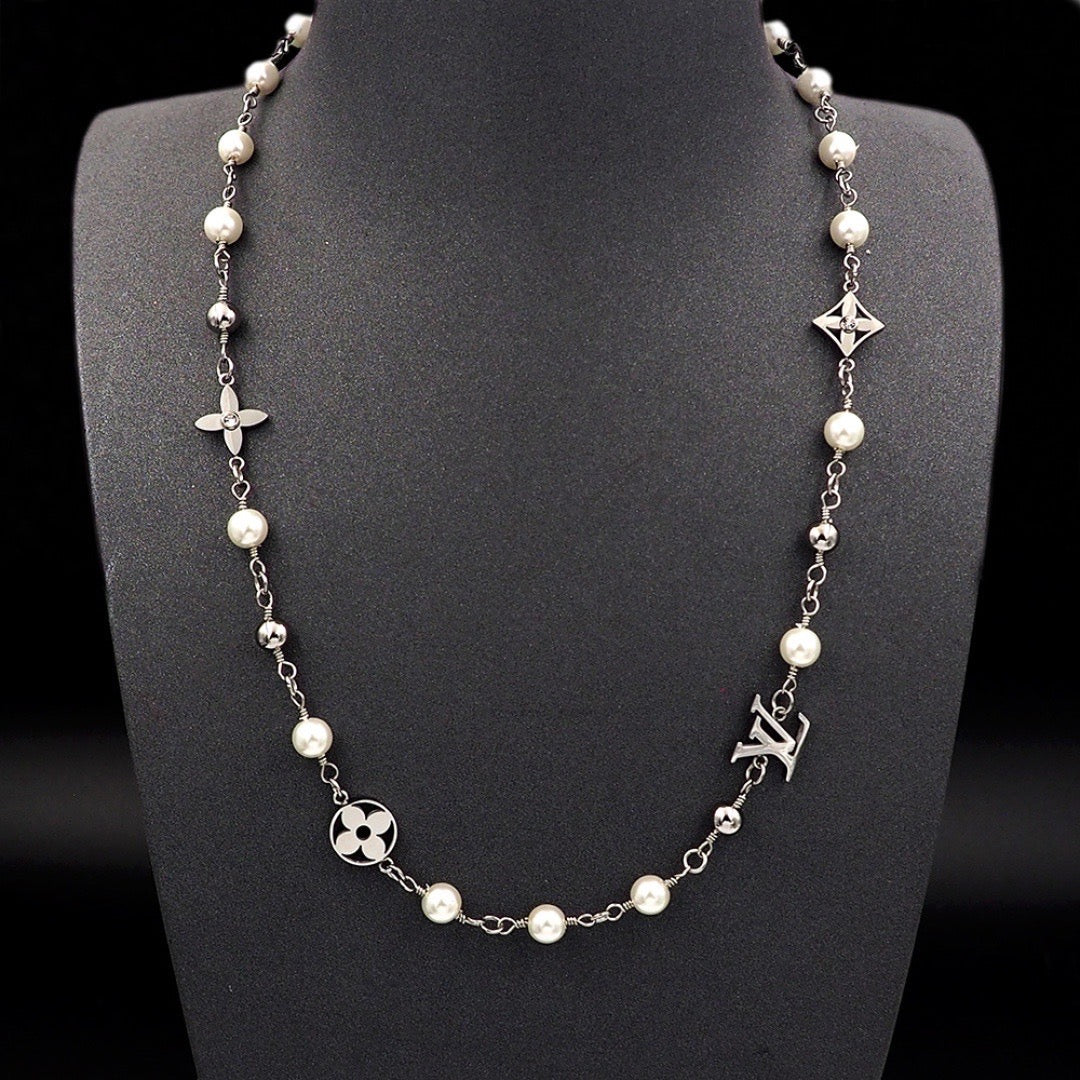 A silver-tone chain necklace with white faux pearls and Louis Vuitton monogram and floral motifs, displayed on a black mannequin bust against a black background.