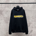 A black Balenciaga hoodie hanging on a black hanger against a textured gray concrete wall. The hoodie features a distressed yellow and white 'SAVANGELISTA' graphic across the chest.
