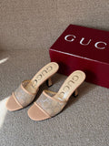 A pair of beige Gucci heeled mule sandals with a tonal GG monogram pattern, displayed next to a dark red Gucci shoebox on a textured gray carpet.