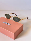 Miu Miu gold-framed sunglasses with dark green lenses resting on a pink textured presentation box against a clean white background.